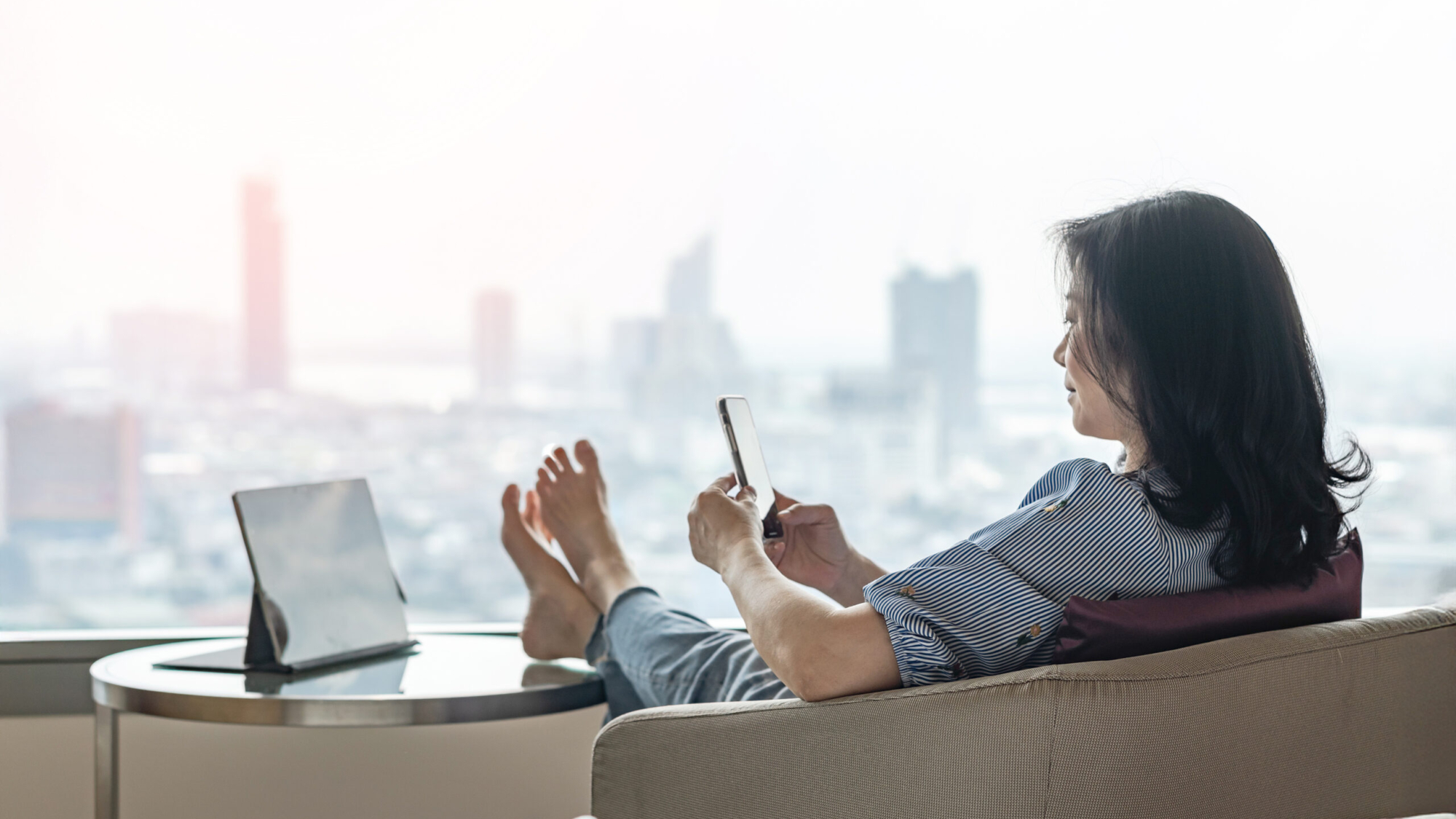 Work-Life balance, life quality, work and travel concept with business woman relaxing sitting in rest, take it easy in modern city hotel guest room or luxury home living room with notebook and smartphone