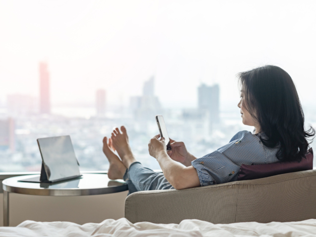 Work-Life balance, life quality, work and travel concept with business woman relaxing sitting in rest, take it easy in modern city hotel guest room or luxury home living room with notebook and smartphone