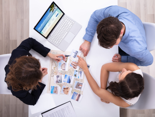 Female Travel Agent Giving Information To A Young Couple For Vacation Package