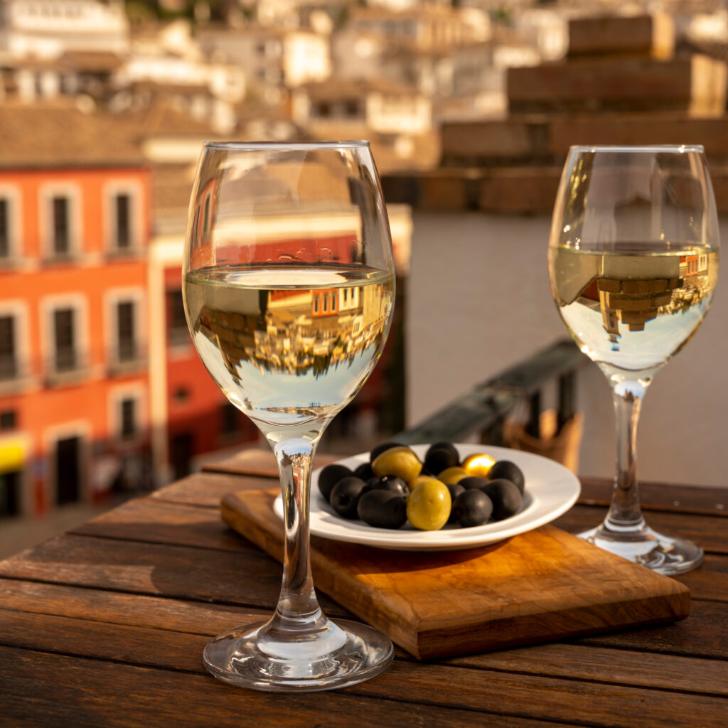 Two glasses of Spanish dry rueda verdejo white wine served with olives on roof terrace with view on old part of Andalusian town Granada, Spain